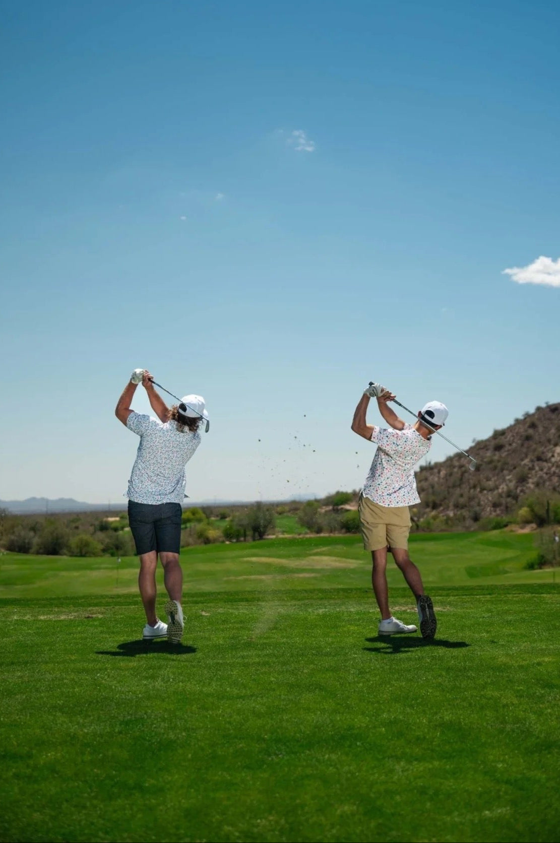 Two people on a golf course with a clear blue sky and mountains in the background.