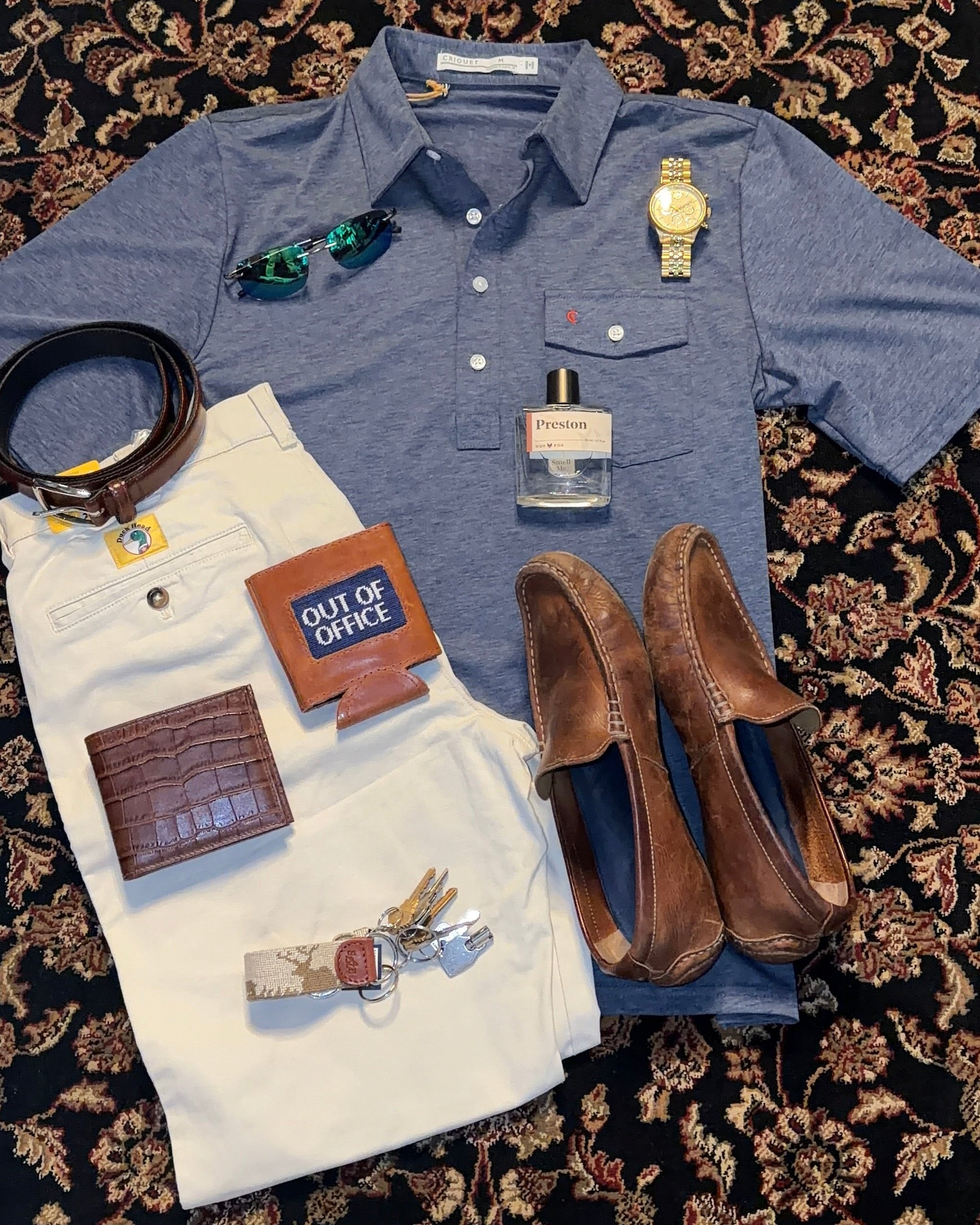 Blue shirt, white pants, brown loafers, and accessories on a patterned rug