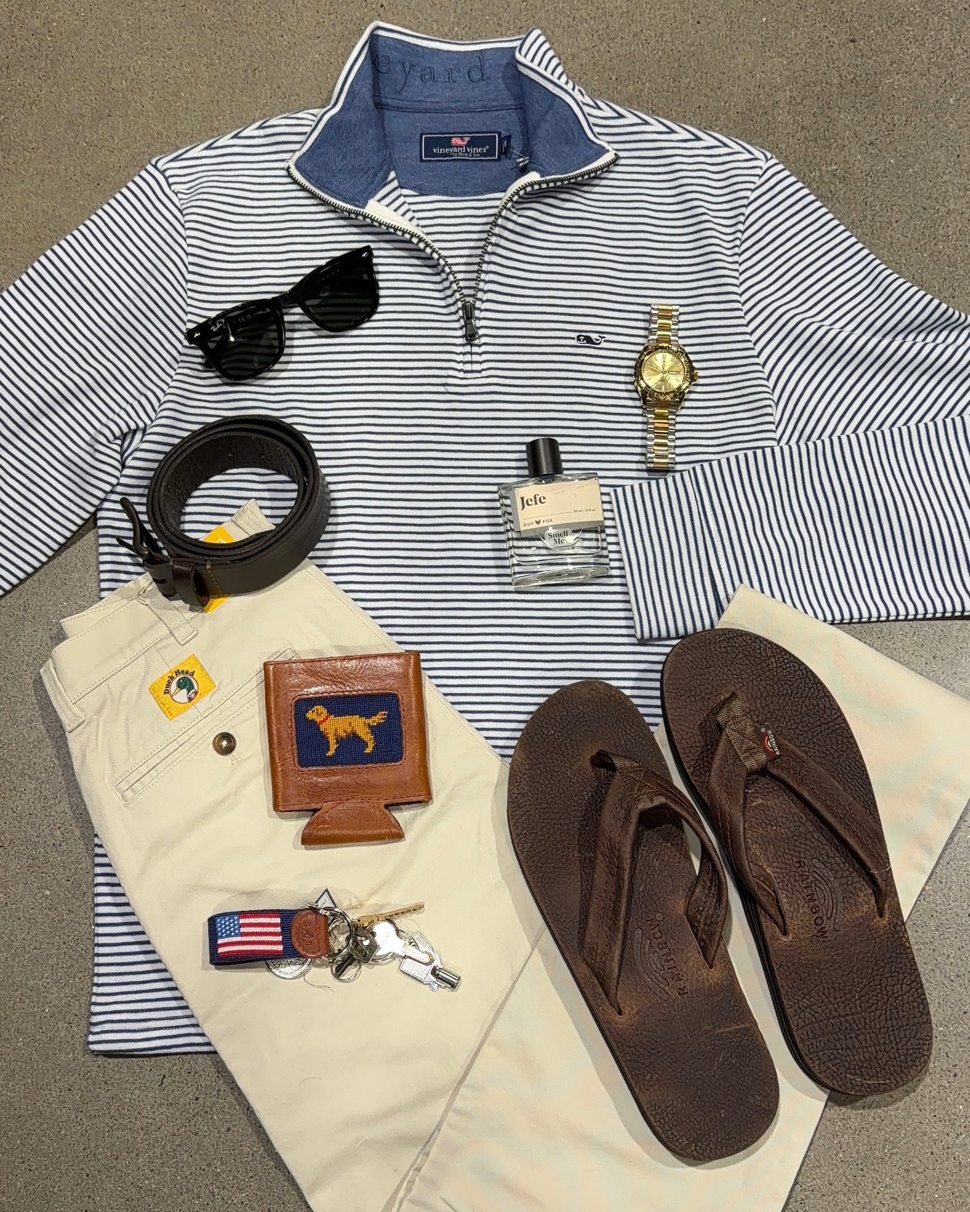 Collection of men's accessories including a shirt, sunglasses, watch, sandals, and a wallet on a gray surface.