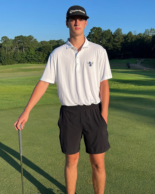 Person on a golf course holding a club with a clear blue sky and greenery in the background