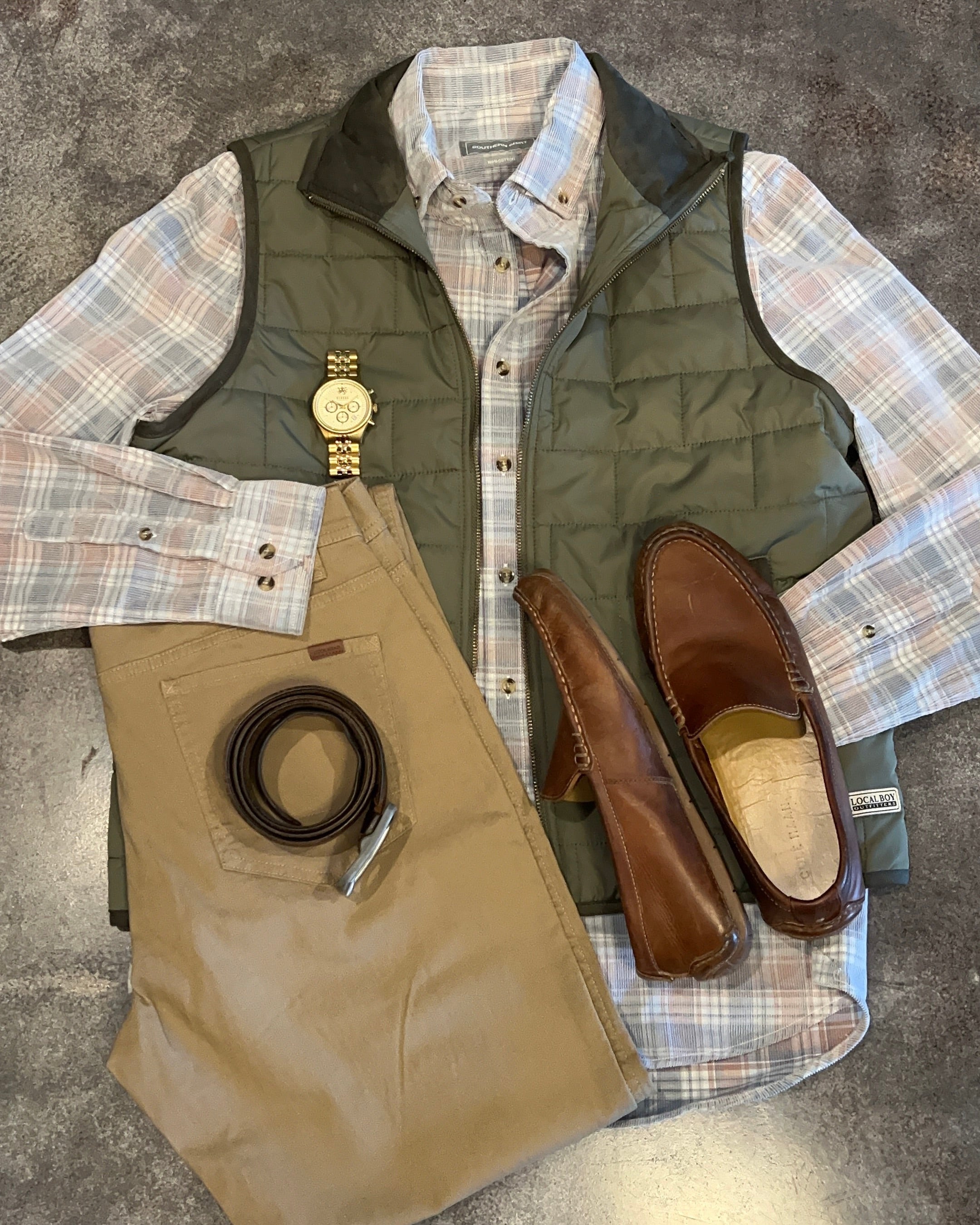 Green vest, plaid shirt, brown shoes, and belt on a gray surface