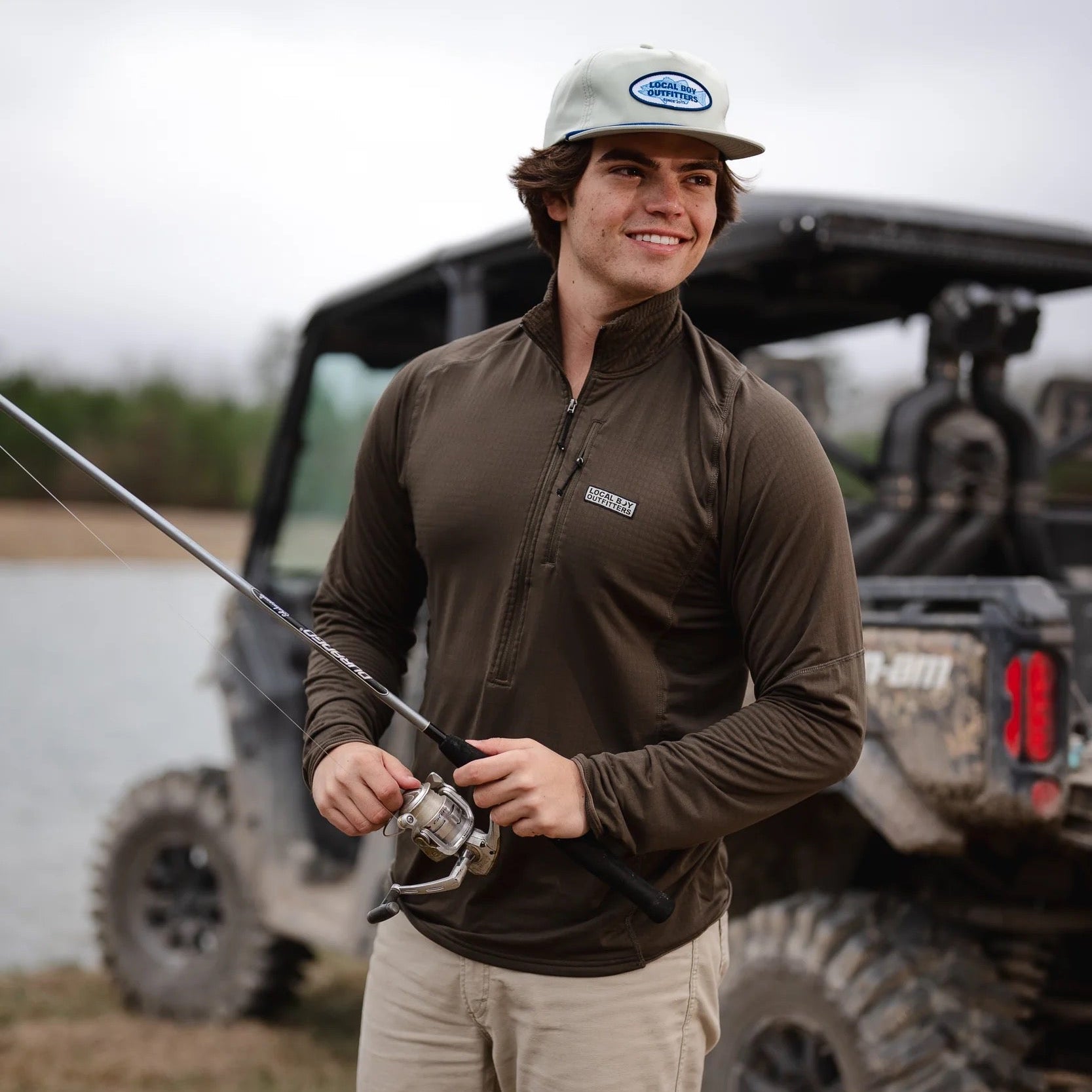 Man holding a fishing rod with an off-road vehicle in the background
