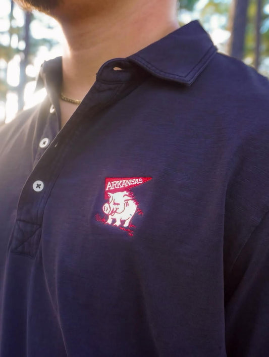 BLACK polo shirt with a red and white logo on a blurred natural background