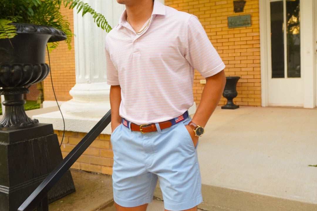 Man standing on steps in front of a brick building wearing a light pink shirt and light blue shorts.